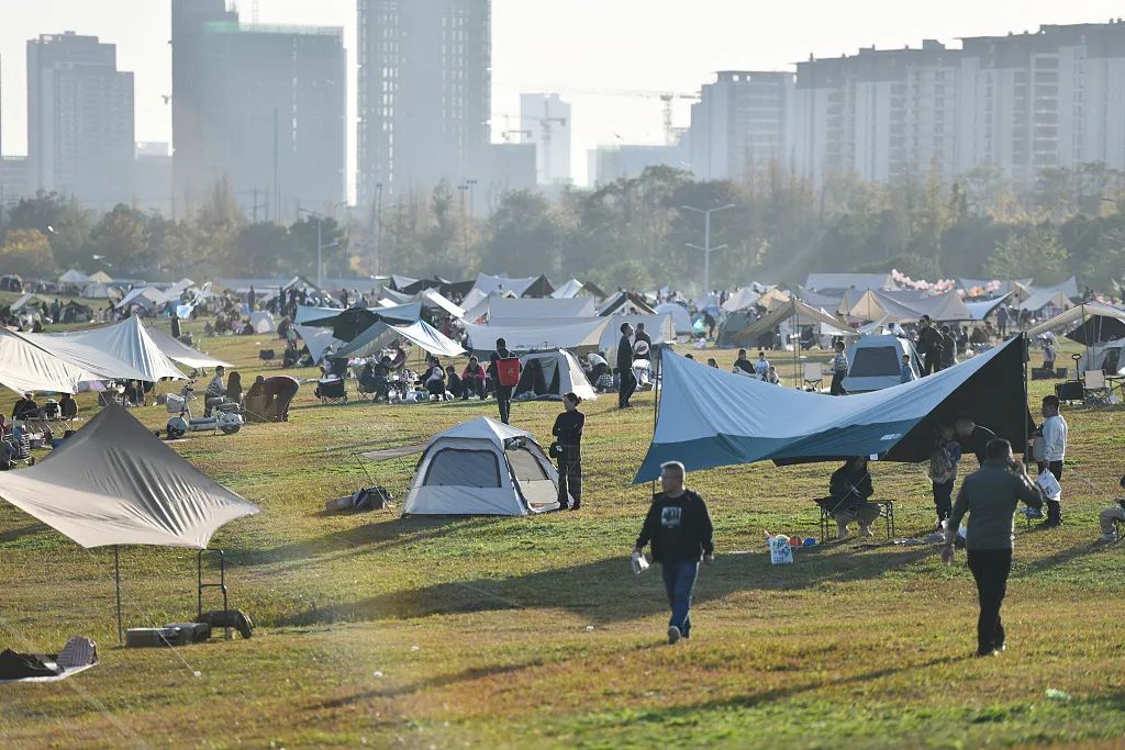 2023年11月26日，初冬的成都迎来晴好天气，气温回升。在成都锦江畔的一块草坪上，“露营大军”在露营区“安营扎寨”晒太阳，打发周末时光。 | 图片来源：视觉中国。摄影：中新社记者 张浪。